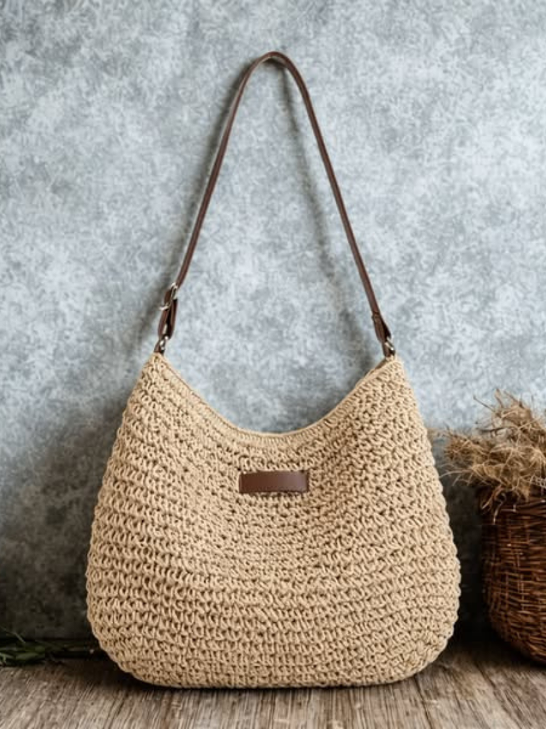 Bolso bandolera hobo trenzado en beige, asa de cuero marrón y cierre rectangular.